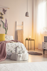 Warm lamp light in a soft colors bedroom interior with a bed dressed in bedding, cushions and...