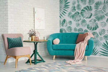 Fotobehang Real photo of turquoise couch and pastel pink armchair standing in bright living room interior with flamingo poster on brick wall and leafy wallpaper © Photographee.eu