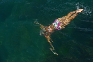 Aged woman is swimming with goggles under green water.