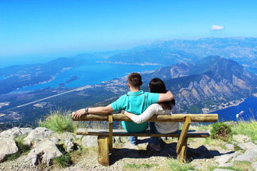 Lovers boy with a girl sit on a bench in the mountains and look at the bay and mountains