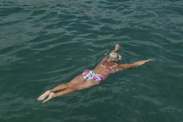 Aged woman is swimming with swim mask in the sea.