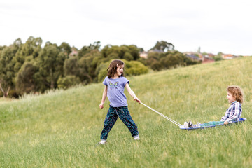 Children grass sledding on a toboggan down a hill in a park