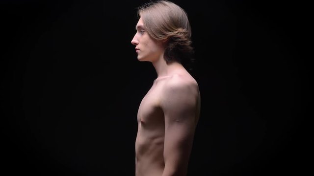 muscular caucasian man standing straight in profile naked in studio on black background