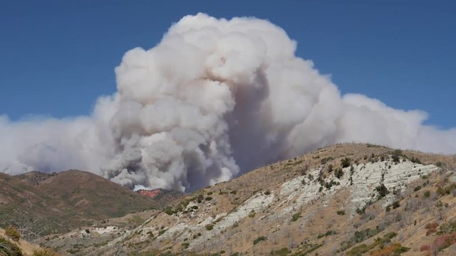 Timelapse-Clouds of billowing smoke churn over hills and red rock cliffs against a clear blue sky as the Pole Creek fire in the Uinta-Wasatch-Cache National Forest in central Utah burns out of control