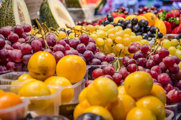 punnets of fresh plums and grapes on sale on a market stall.