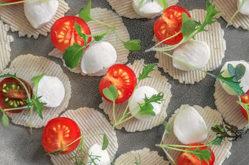 Mozzarella and tomatoes with thyme, arugula and Basil are on corn chips. Preparation of canapes.