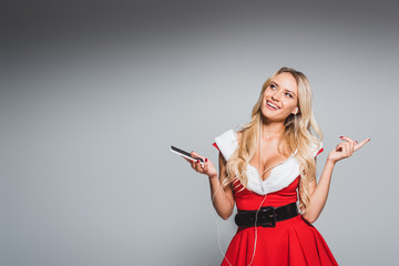 dreamy santa girl in christmas dress listening music in earphones with smartphone isolated on grey background