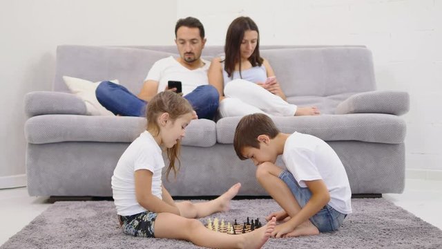 child play chess on floor at home. parents using the phones on the backgroud