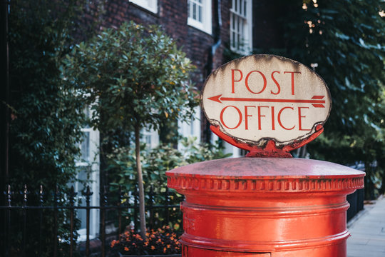 Red Post Box With A Retro Post Office Directional Sign On Top In London, UK.