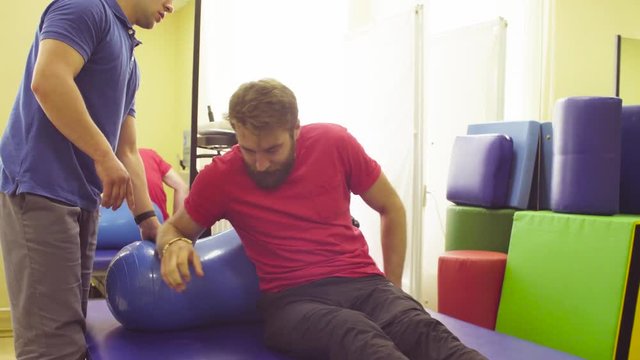 Disabled young man doing recovery exercises in a rehabilitation clinic. Doctor physical therapist helping him.