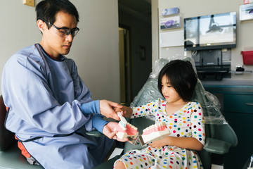 Asian girl practices tooth brushing while sitting in dental chair