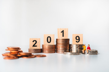 Miniature people, couple woman sitting on golden stack coins with mini house and year 2019 using as business, financial and property concept