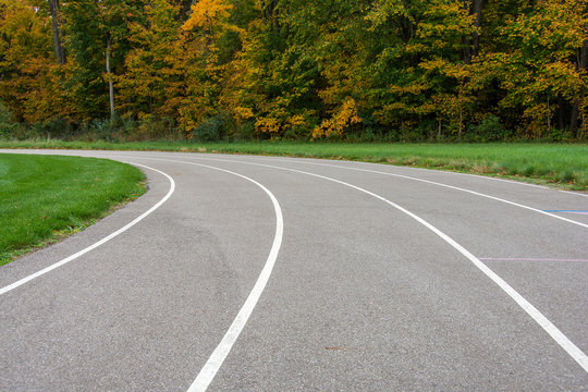 vacant sports track with white lines curving into autumn trees