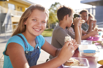Girl at elementary school lunch table smiling to camera