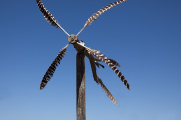 MOTION BLUR. Weathervane feather-vane against blue sky. Handmade with bird feathers.