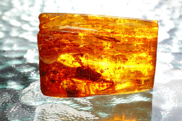 Amber. A bright luminous piece of amber on a background of waves. Fossil resin as a natural material for jewelry. Sunstone. Natural mineral. Crystal. Ancient vintage jewelry. Amber with insect inside