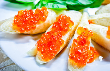 Naklejka na ściany i meble Pancake with red caviar served on white plate with green leafs.