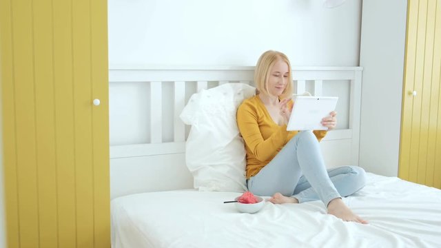 Beautiful vegan woman is sitting on the bed and surfing internet on tablet pc.