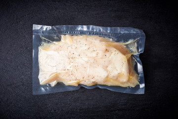 Chicken breast vacuum sealed on black table, from above