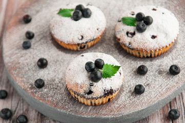 Blueberry muffins which are decorated with powdered sugar, blueberries and mint. Photo in a rustic style on a wooden background. Blurred.