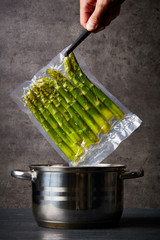 Hand holding asparagus over cooking pot