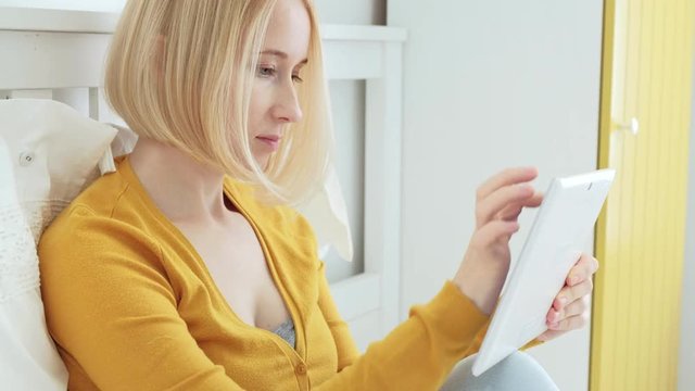 Portrait of attractive blonde Caucasian woman smiling and using digital tablet.