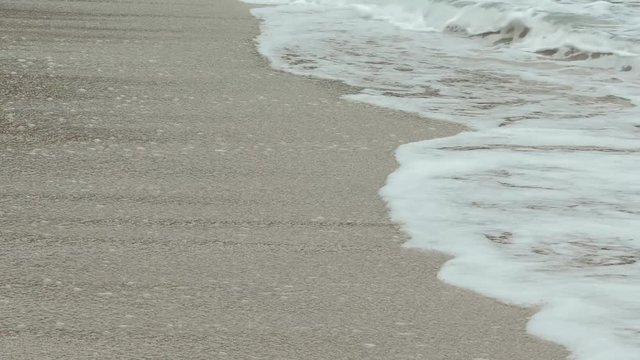 Sea waves crash over the sand beach on cloudy day