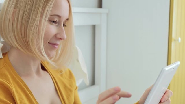 Portrait of attractive blonde Caucasian woman smiling and using digital tablet.