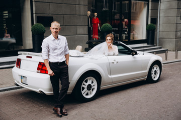 A newlyweds trip in the car. The groom invites the bride in a white cabriolet.
