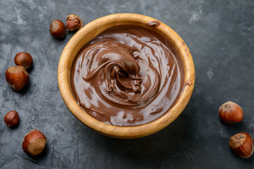 Chocolate cream in a bowl, nuts  and chocolate pieces on dark table.