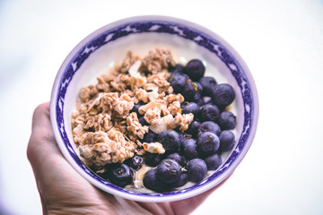 A hand holding a smoothie bowl with granola and blueberries on a white background.