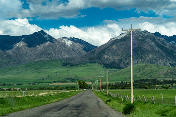 Paved road with power lines leading into the Absaroka Mountain Range in Montana's Paradise Valley, located in Park County, Montana, on a partly cloudy spring day