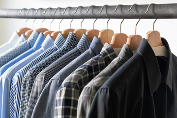 Row of men's shirts in blue colors on hanger on white background