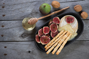 Melted camembert served with grissini, slices of fig fruits and honey. Top view on a grey rustic wooden background, horizontal shot