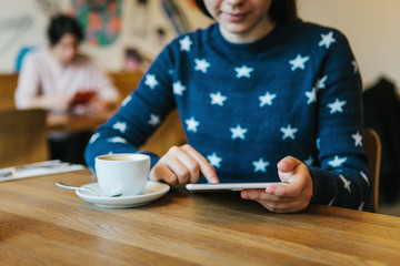 A girl in a cafe drinks coffee and uses a tablet.