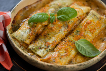 Close-up of cannelloni baked with spinach and cheese and topped with fresh green basil, studio shot