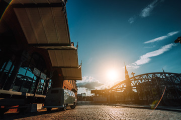 Beautiful retro style car packed on the cobbled square. Arch bridge over canals with Sankt Katherinen church in the background. Warehouse district in Hamburg, Germany. Warm sunset light. Revival style