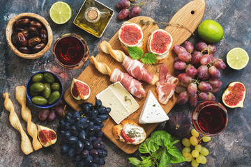 A variety of snacks, prosciutto,grapes, wine, cheese with mold, figs, basil, olives on a rustic background. Top view,flat lay