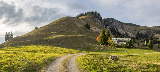 Panorama einer grünen Alm mit Hütte am Berg vor bewölktem Himmel bei letzter Abendsonne, Bayern