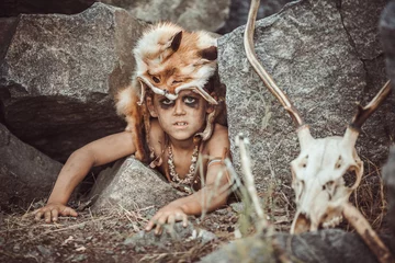 Aluminium Prints Hunting Caveman, manly boy hunting outdoors. Prehistoric tribal boy outdoors on nature. Young shaggy and dirty savage, warrior and hunter hiding in an ambush behind a stone in cave. Primitive ice age man in