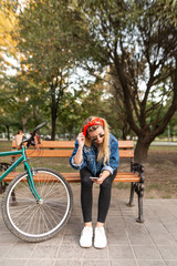 Stylish girl sitting on the bench in the park, with a bike and using a smartphone. A woman uses an internet connection on a smartphone while walking in the park.