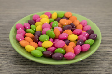 Many colored candies on a green plate on a wood table