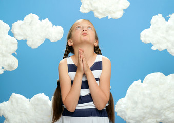 girl dressed in striped dress posing on a blue background with cotton clouds, looking up and dreaming, prays, the concept of summer, holiday and happiness