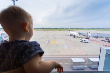 A little boy looks out the window at the airport on the airplanes. Family travel and adventure.