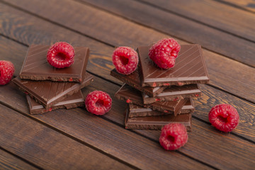 A stack of chocolate bars with built-in red raspberry berries. Fresh raspberries and chocolate on wooden background.