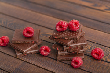 A stack of chocolate bars with built-in red raspberry berries. Fresh raspberries and chocolate on wooden background.