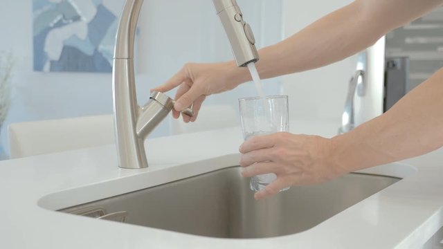 man pouring water from the faucet in glass in a modern kitchen