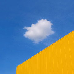 New yellow metal panel construction, wall of building with blue sky and white cloud in background