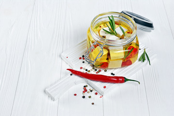 Marinated feta cheese with olive oil and spice of red chili pepper and rosemary in glass jar