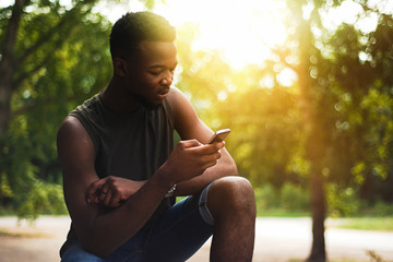 Hipster, a young man using a smartphone. African American teenager holding a mobile smartphone at sunset